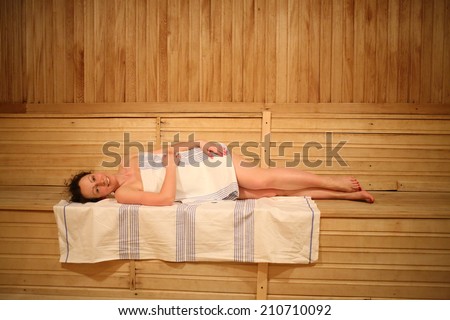 Beautiful young woman relaxing on a shelf in a spacious sauna