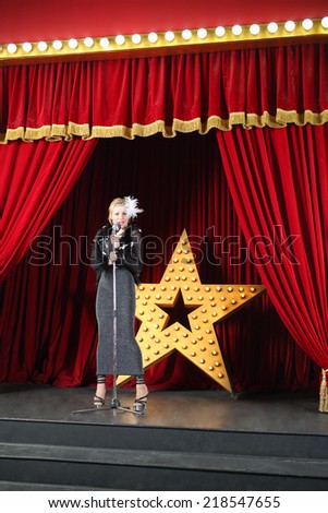 Beautiful singer in long black dress performing on stage at music hall
