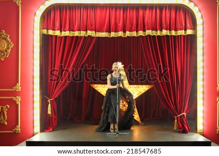 Beautiful young singer in black dress stands on red stage