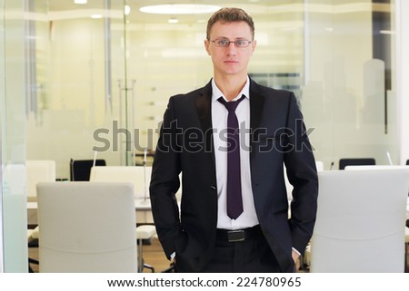 Young businessman in black suit stands with hands in pants in conference room