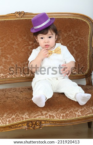 Little boy in white suit and purple hat sitting on couch