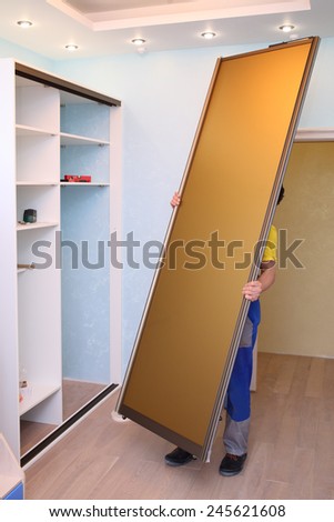 Worker holding door for sliding wardrobe in room with blue walls
