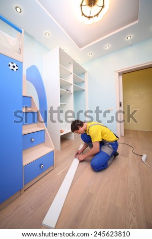 Young man sitting on the floor secures door sliding wardrobe in room with blue walls