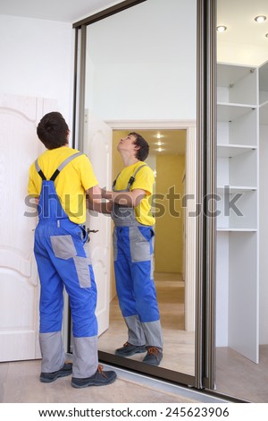 Young man fixing mirrored doors on corner sliding wardrobe in room