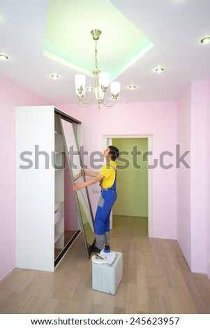 Worker setting mirrored doors for sliding wardrobe in room with pink walls
