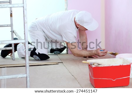 Finisher in white clothes with a brush in hand painted walls in pink room near the floor