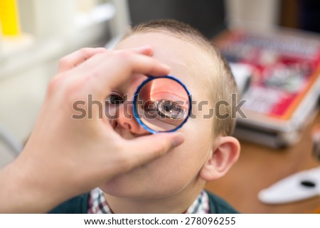 ophthalmologist examines the eyes of a boy through a magnifying glass
