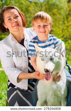 Mom with laughing son and dog sitting on grass in summer park