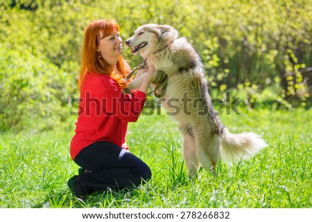 woman in red sweater and red hair smiling and playing with dog in park