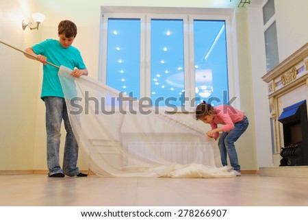 Brother and sister together hanging curtains in new apartment in evening
