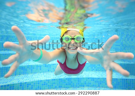 Portrait of happy girl in swimming glasses under water in the pool