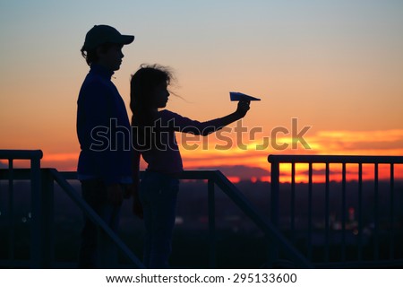brother and sister let paper plane from roof of multistory home late at night, silhouettes