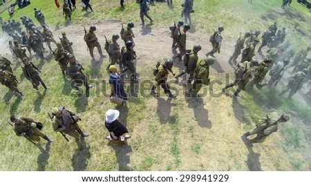 RUSSIA, NELIDOVO - JUL 12, 2014: Civilians and soldiers in uniform of soviet army walk in dust on road during reconstruction Battlefield at sunny day. Aerial view. Photo with noise from action camera