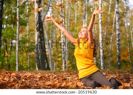 Beauty blond girl throws leaves in the park in autumn