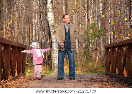 Grandfather with  granddaughter  on wooden bridge in wood in autumn throw leaves