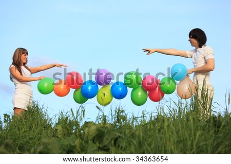 girl and guy hold garland of multicolored balloons in grass against sky