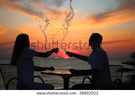 silhouettes of man and woman splash out drink from glass on sea sunset