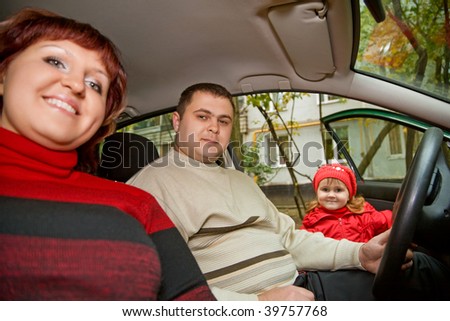 Married couple and  little girl sit in car near a building
