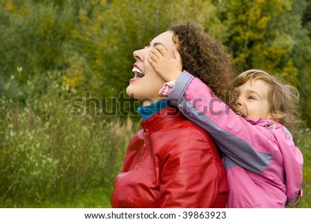 young woman and little girl playing in garden, girl closes eyes to mother