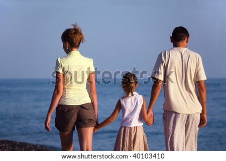 Family with girl walks along sea beach. Back view.