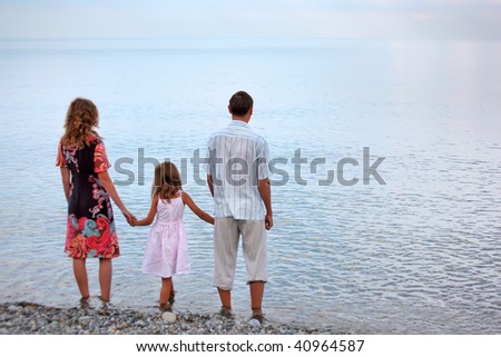 Happy family with little girl standing on beach in evening, standing back