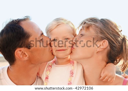 Happy family with little near to sea, parents kiss daughter