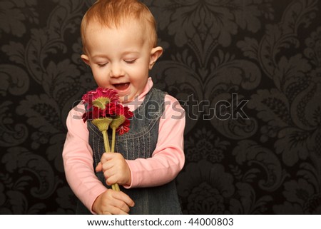 Portrait of little girl with flowers in her hands against ornamental wall.