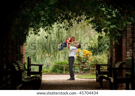 Father and daughter in summer garden  in plant tunnel. Man plays with girl lifting her on hands.