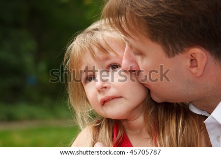Sad little girl cries in park. Father calms her kissing on cheek.  Close up.