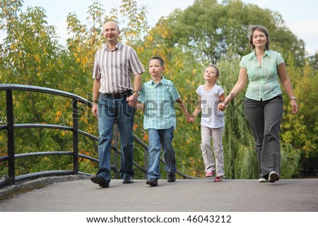 mom, dad, son and daughter is walking on bridge in early fall park. family is handies.