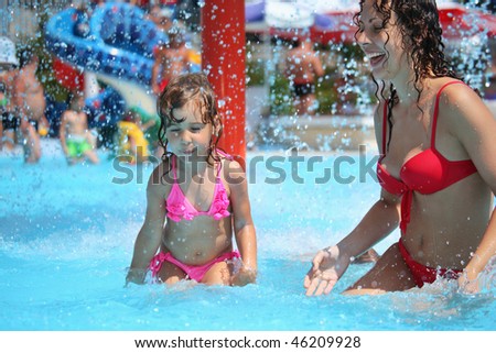 Smiling beautiful woman and little girl bathes in pool under water splashes