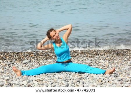 joyful woman wearing sporty clothes is making exercise on sea coast. she is stretching