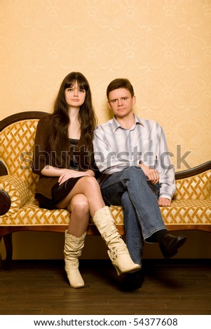 young beautiful woman and young man sitting on sofa in room, combined hands in lap