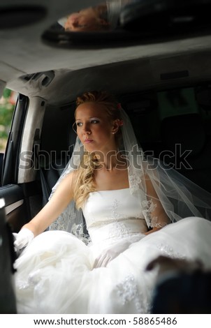 Bride in wedding dress sits in limousine and looks out in window.