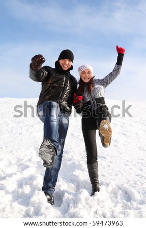 young man and girl stand on snowy area and put one leg up, looking at camera