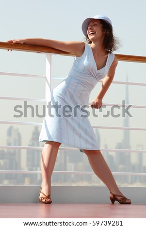 young beauty brunette woman standing on cruise liner deck, hand on rail, city on background