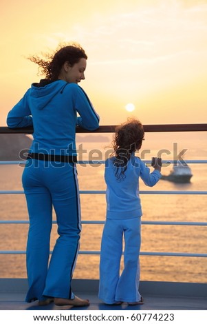 beautiful woman and her daughter both wearing tracksuits are standing on deck of ship and looking at setting sun. ship in out of focus.