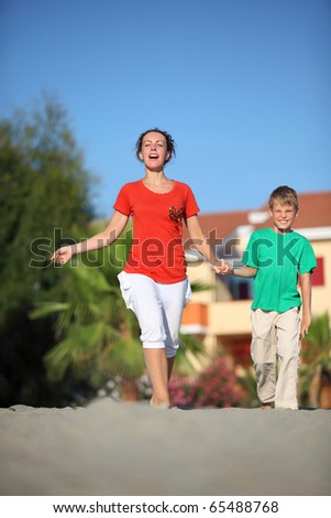 Woman with  son holding on to hands hurry on  beach by  bright sun day