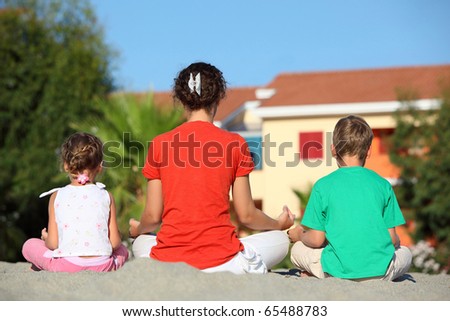 Mother with two children turned the backs, sit in  pose of yoga and meditate