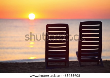 Two empty dark blue chairs stand on  beach in  evening with  view on marine sunset