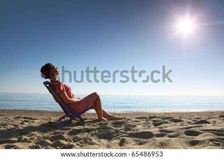 Woman sits on  plastic chair on  sea-shore by  person to  sun and becomes tanned, heaving up  head