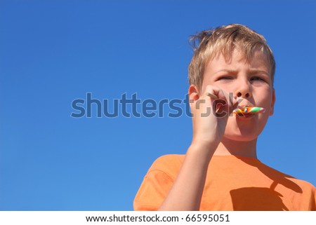 little boy in orange shirt eating multicolored lollipop, blue sky