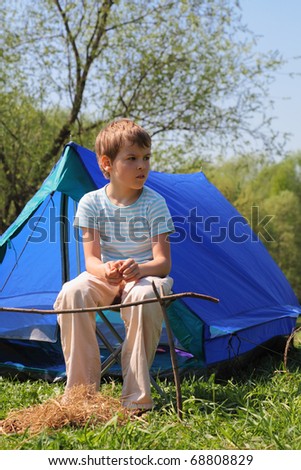 little boy in striped shirt sitting near blue tent on nature