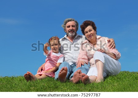 barefooted old man and woman sitting on lawn with their granddaughter, girl pointing by finger