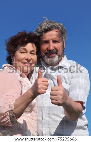 old man and woman making thumbs up gesture, blue sky