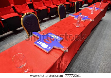 Long judge table with  red table-cloth on which cards lie stands in empty hall