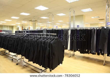 rows of jackets and men trousers on hangers in big light shop