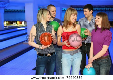 Five friends stand with balls for bowling and look on each other, focus on girl in center and on right