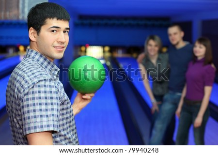One fellow stands sideways and holds ball for playing in bowling and three friends hearten him, focus on  man