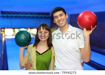 Man and young woman hug and in free hand hold  ball for bowling